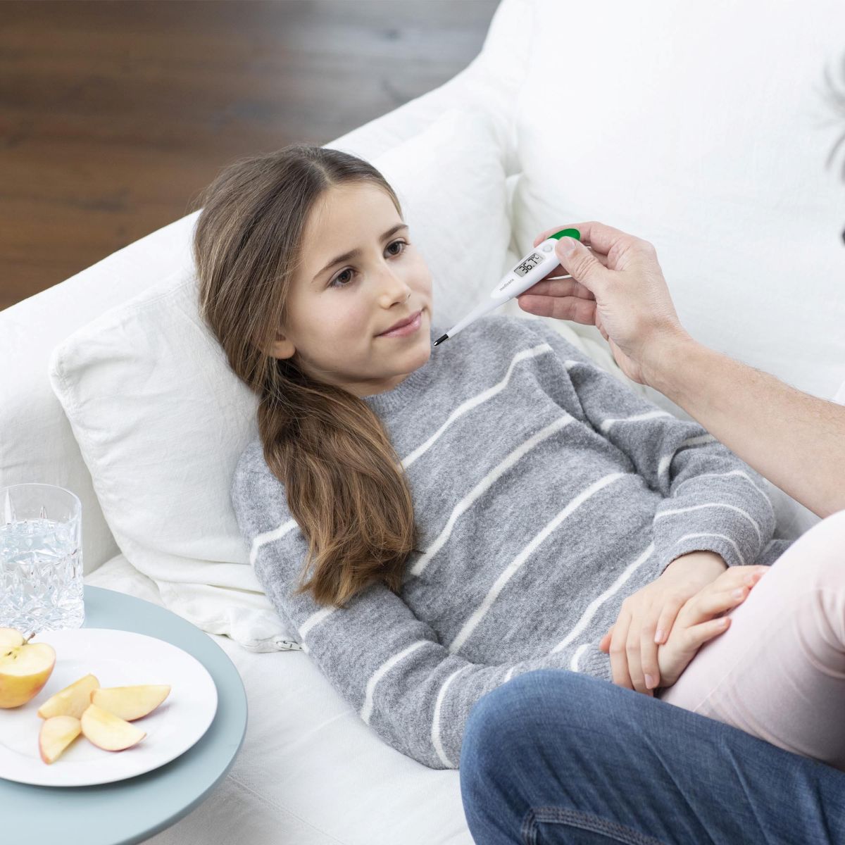 Child lying on the sofa while an adult measures the temperature with a Medisana digital thermometer.